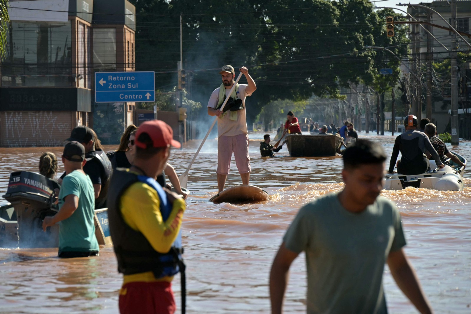De cima a baixo, equipes de resgate vasculham prédios em Porto Alegre em busca de habitantes presos em apartamentos ou telhados. No centro da foto, homem se locomove na rua inundada com prancha de Stand Up. — Foto: NELSON ALMEIDA / AFP