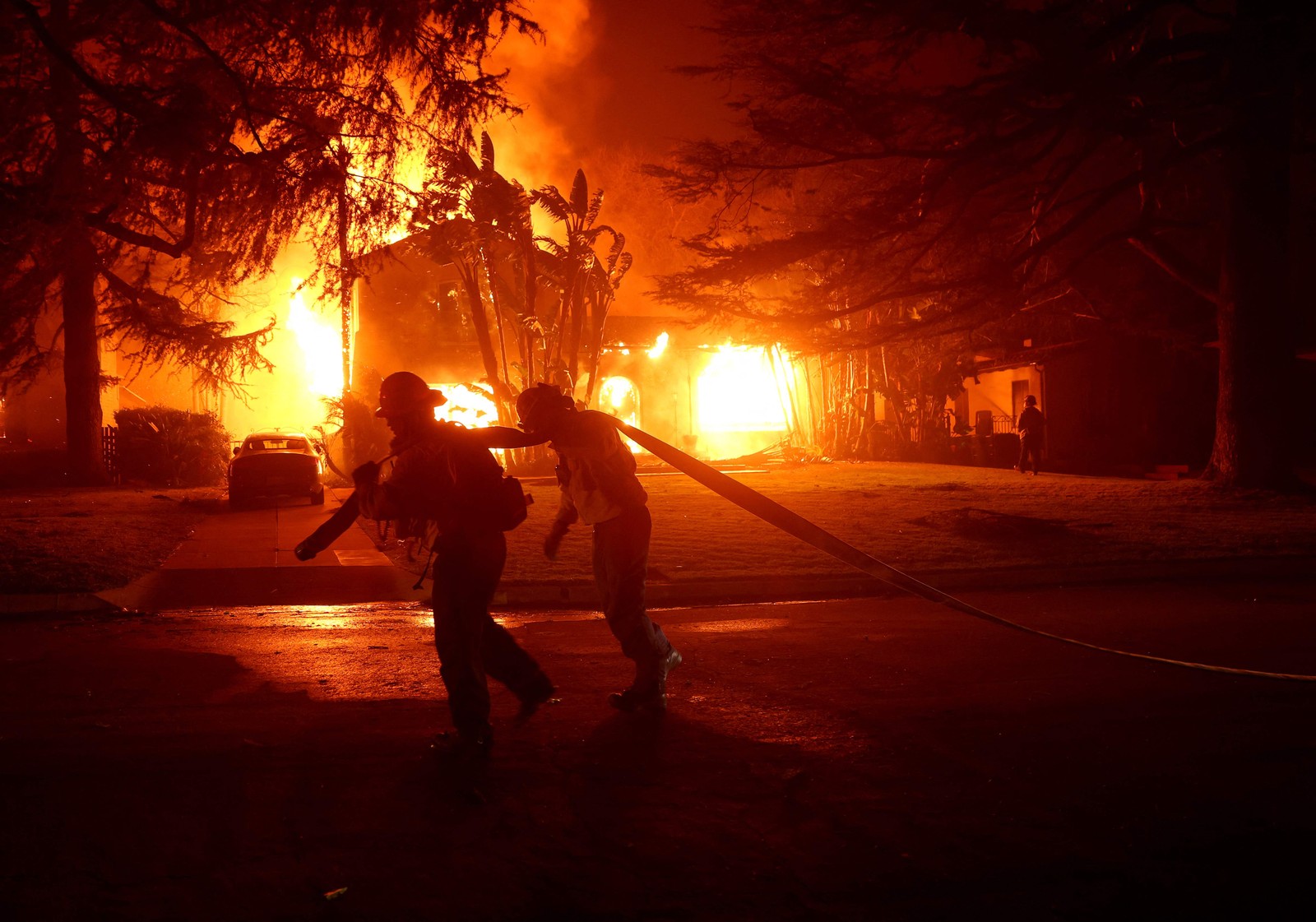 Bombeiros combatem incêndio em frente a uma casa em chamas em Los Angeles, em 8 de janeiro de 2025 — Foto: Justin Sullivan/Getty Images/AFP