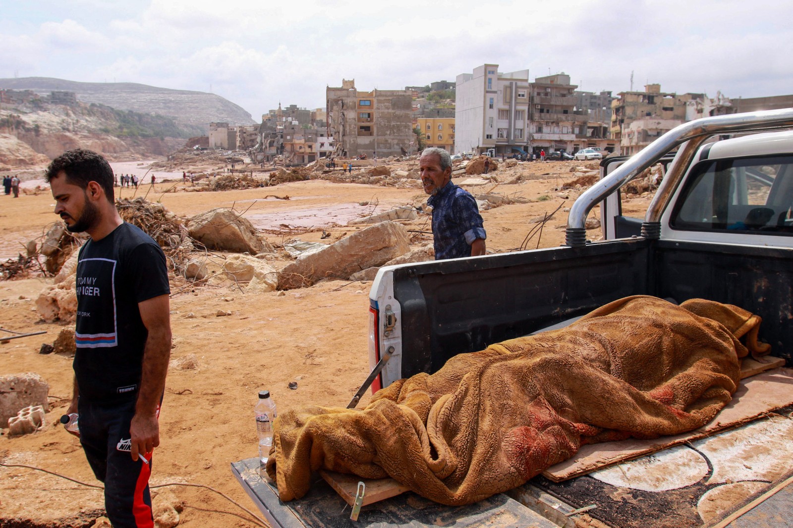 Pessoas passam pelo corpo de uma vítima de enchente na traseira de uma caminhonete em Derna, leste da Líbia — Foto: AFP
