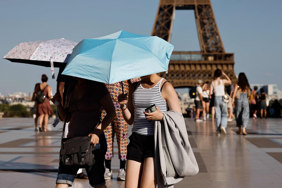Turistas se protegem do som com guarda-chuvas aos pés da Torre Eiffel — Foto: Ludovic Marin/AFP
