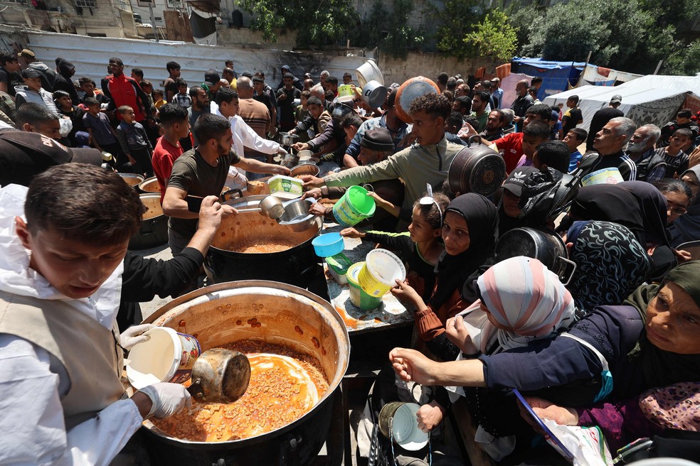 Palestinos fazem fila para receber porção de comida distribuída por cozinha beneficente no campo de refugiados de Nuseirat — Foto: Eyad Baba/AFP