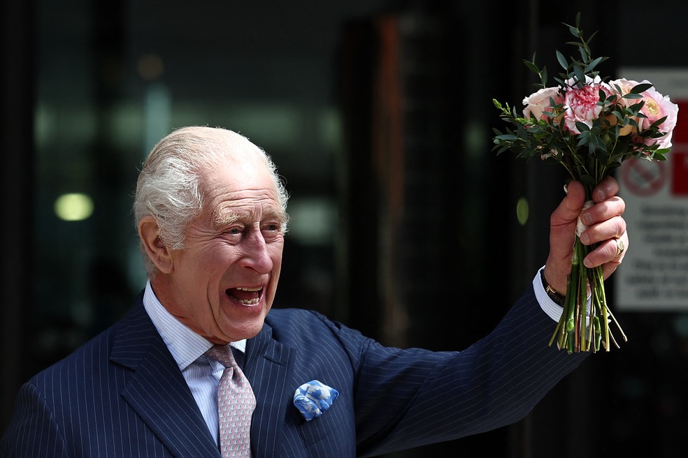 O rei Charles III acena e balança um buquê de flores durante sua visita ao Centro de Câncer Macmillan do Hospital Universitário de Londres. — Foto: HENRY NICHOLLS/AFP