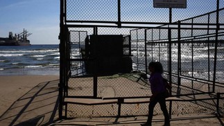 Uma mulher passa por dutos em Puerto Ventanas. Polo industrial abriga quatro termelétricas a carvão e refinarias de petróleo e cobre — Foto: PABLO VERA / AFP