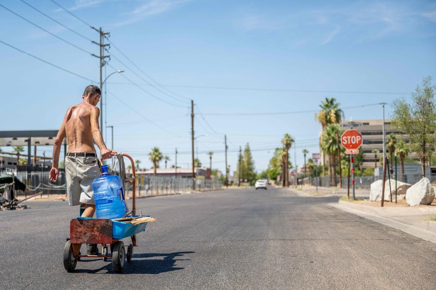 Homem carrega galão de água em Phoenix, no Arizona, em meio ao calor escaldante