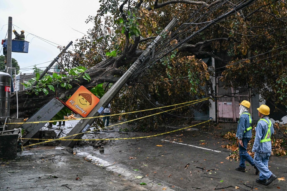 Workers inspect fallen poles and trees on a street in Quezon City, Metro Manila — Photo: Jam Sta Rosa/AFP