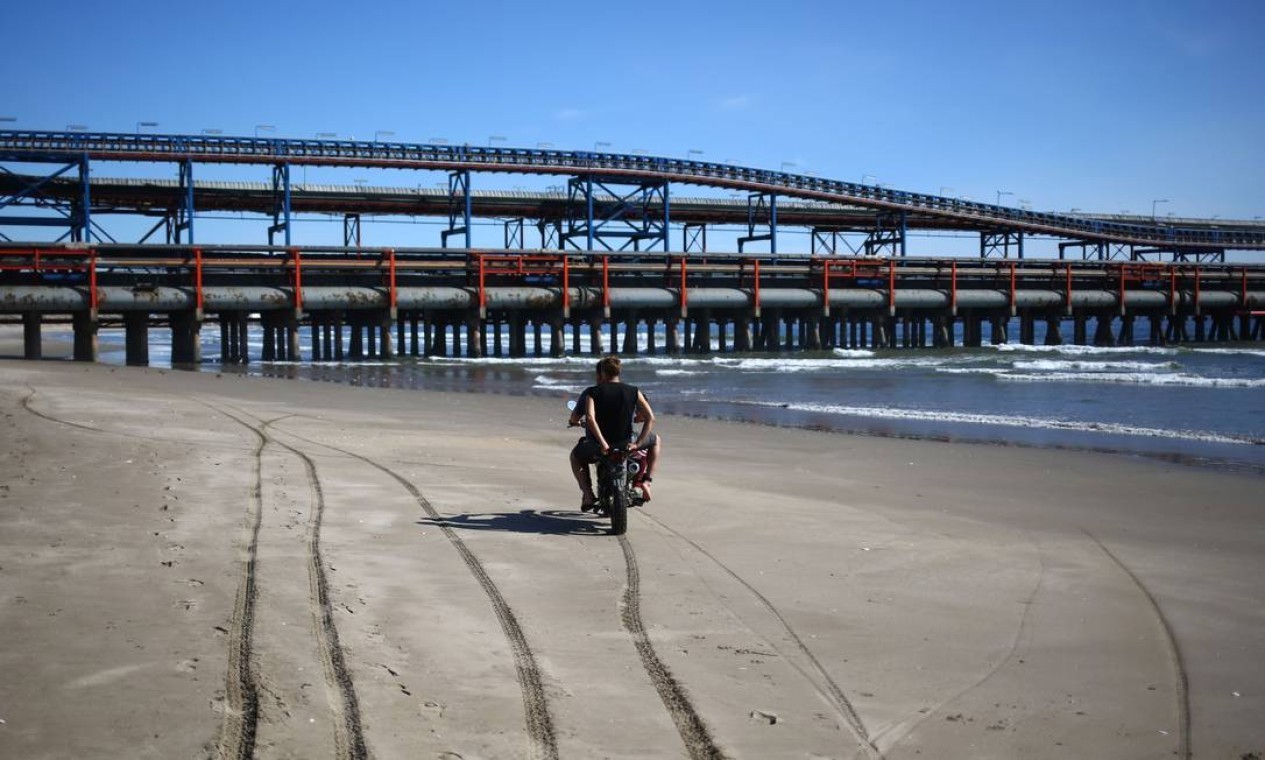 Adolescentes andam de moto perto de tubulações em Puerto Ventanas. "Chernobyl chilena", como é chamado pela organização Greenpeace, expõe a população, especialmente crianças e grávidas, a episódios recorrentes de intoxicação e doenças crônicas — Foto: PABLO VERA / AFP