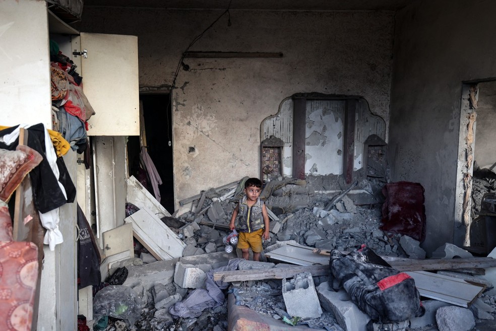 Uma criança palestina segura um carrinho de brinquedo que recuperou dos escombros de uma casa destruída por um ataque israelense, no campo de refugiados de Nuseirat, no centro da Faixa de Gaza — Foto: Eyad BABA / AFP