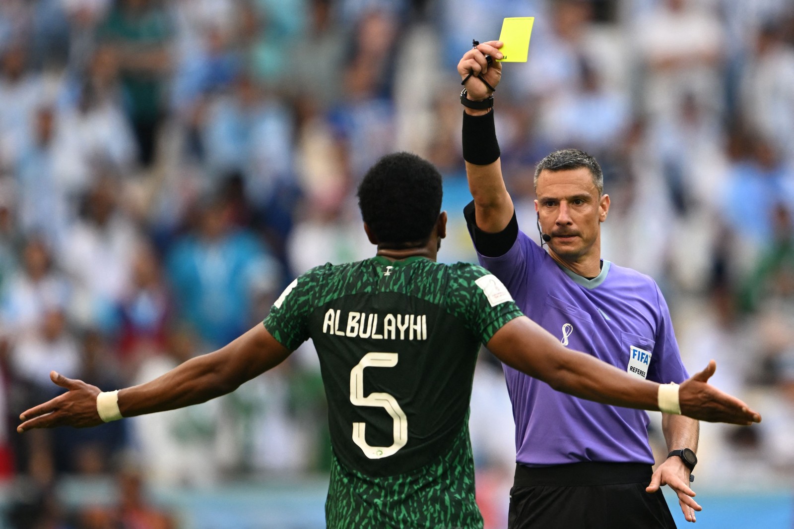 O árbitro esloveno Slavko Vincic mostra um cartão amarelo ao zagueiro Ali Al-Bulaihi, da Arábia Saudita — Foto: Kirill KUDRYAVTSEV / AFP