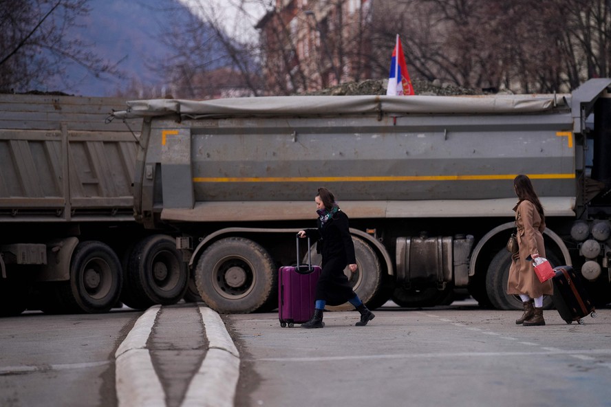 Pedestres passam por uma nova barricada montada na cidade dividida de Mitrovic, na fronteira entre Kosovo e Sérvia