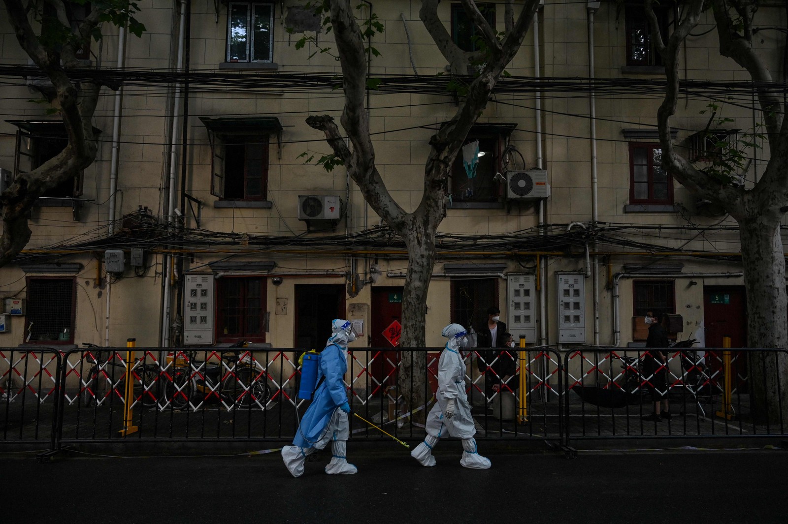 Trabalhadores que pulverizam desinfetante caminham por uma rua próxima a uma área residencial sob um bloqueio Covid-19 no distrito de Huangpu, em Xangai — Foto:  HECTOR RETAMAL / AFP