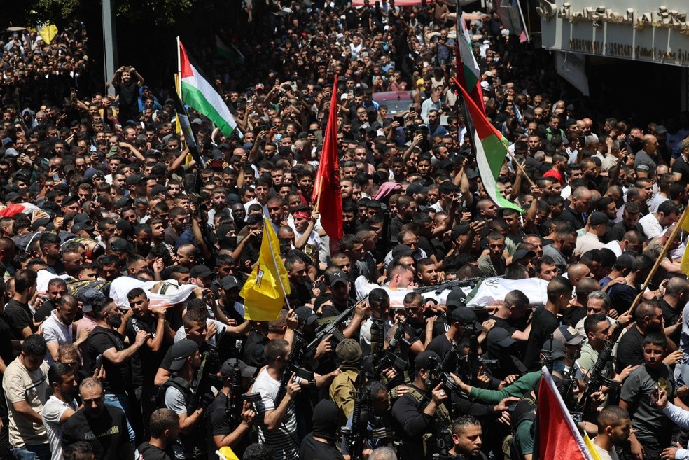 Multidão carrega caixões de mortos durante ofensiva israelense — Foto: Ahmad Gharabli/AFP