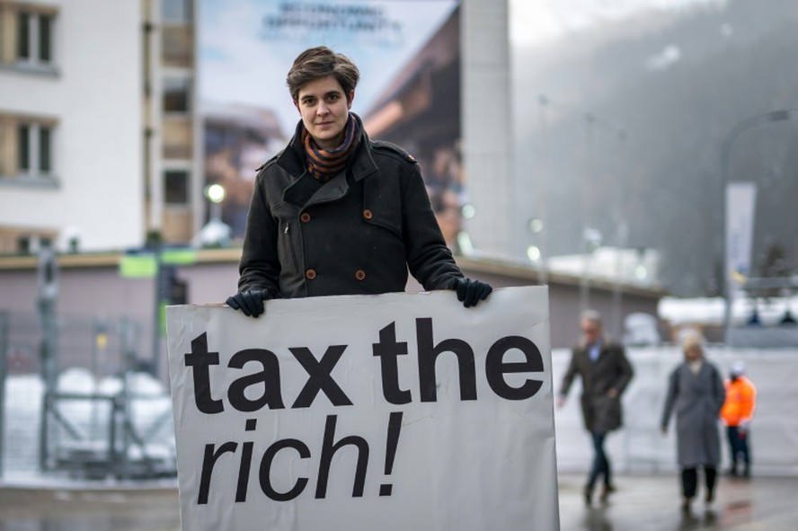 A bilionária austríaca Marlene Engelhorn posa com uma placa que diz 'Taxe os ricos!' na entrada do centro de congressos em Davos