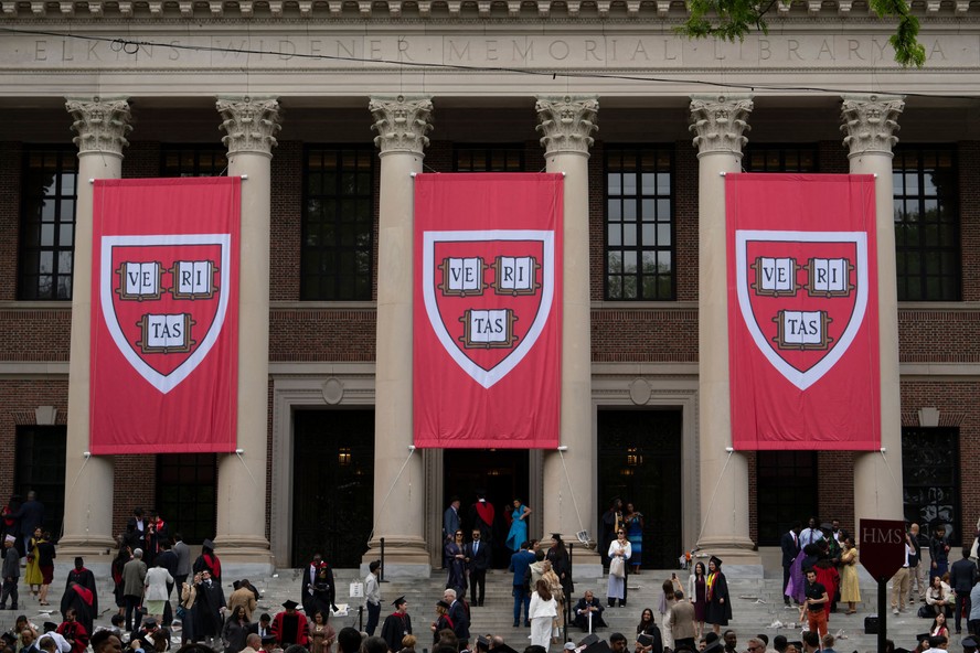 Bandeiras com o símbolo de Harvard adornam um dos prédios da universidade que se tornou símbolo da resistência da ciência aos ataques de Trump