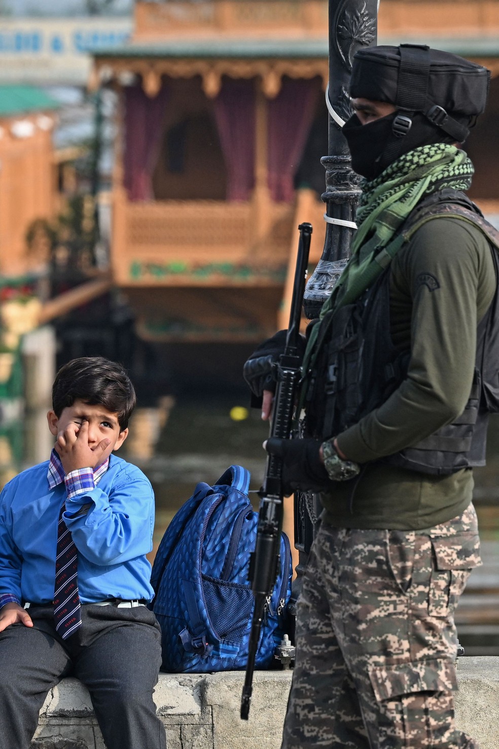 Criança senta-se às margens do Lago Dal enquanto um paramilitar indiano patrulha Srinagar — Foto: Sajjad HUSSAIN / AFP