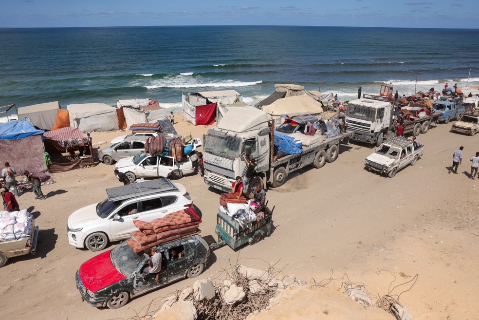 Palestinos carregando pertences chegam a uma trilha costeira a noroeste do campo de refugiados de Nuseirat, enquanto são deslocados para o sul de Gaza após o anúncio israelense de fechar a estrada al-Rashid — Foto: Bashar TALEB / AFP