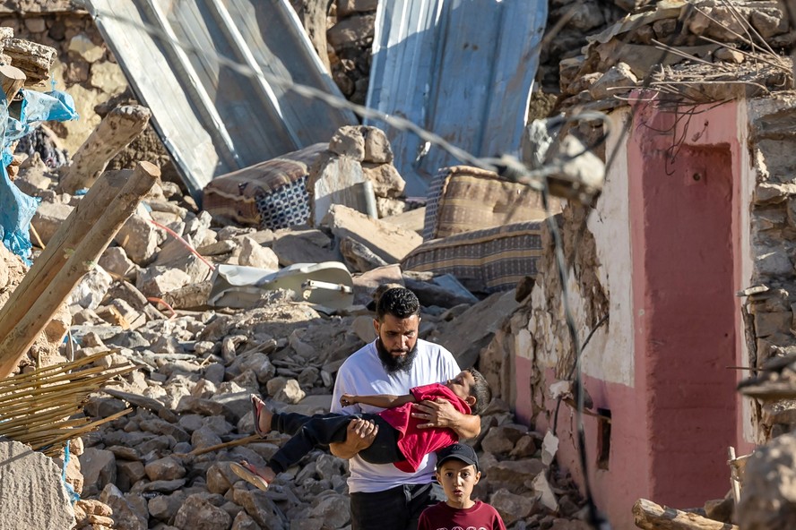 Morador carrega criança no meio das casas destruídas na vila montanhosa de Tafeghaghte, a sudoeste de Marrakesh