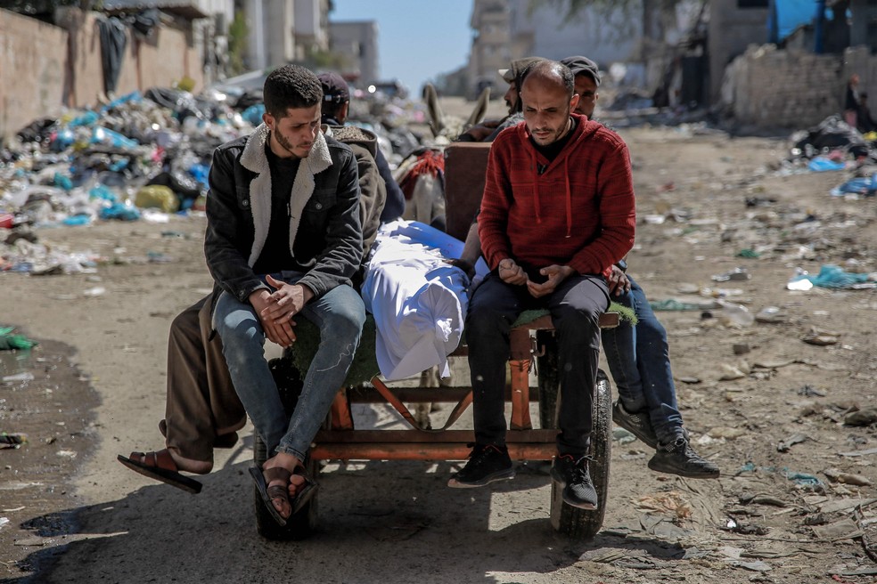 O corpo de um palestino morto é transportado em uma carroça puxada por um burro em 29 de fevereiro. O ministério da saúde em Gaza, controlado pelo Hamas, disse que as forças israelenses mataram a tiros dezenas de pessoas quando uma multidão correu em direção a caminhões de ajuda. Fontes israelenses confirmaram que as tropas abriram fogo contra os palestinos, com uma delas dizendo que os soldados pensavam que eles "representavam uma ameaça" e que muitos morreram quando foram atropelados por caminhões de ajuda — Foto: Omar AL-QATTAA / AFP
