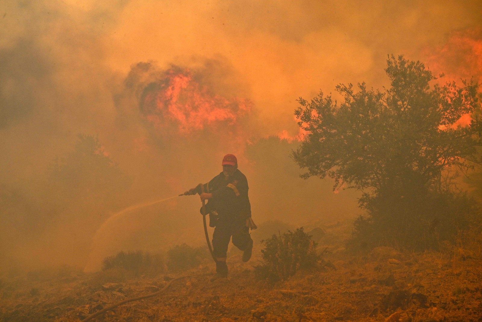 Um bombeiro foge das chamas enquanto tenta controlar um incêndio florestal em New Peramos, perto de Atenas.  — Foto: Louisa GOULIAMAKI/AFP