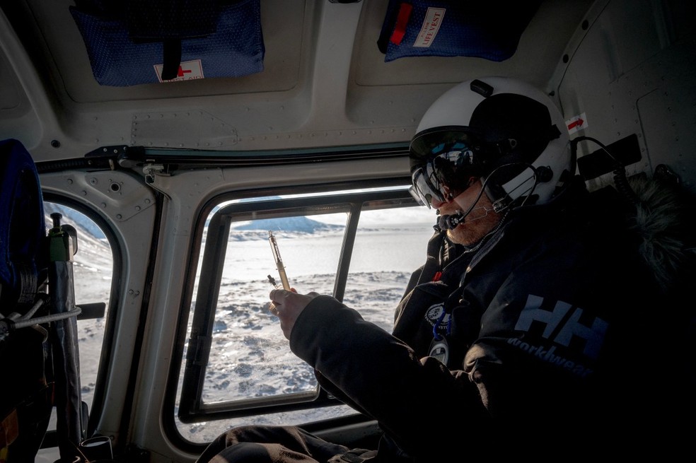 O veterinário norueguês Rolf Arne Olberg carrega seu rifle de ar comprimido com um dardo para sedar ursos polares em um helicóptero sobrevoando o gelo marinho no leste de Spitzbergen, no arquipélago de Svalbar — Foto: OLIVIER MORIN / AFP
