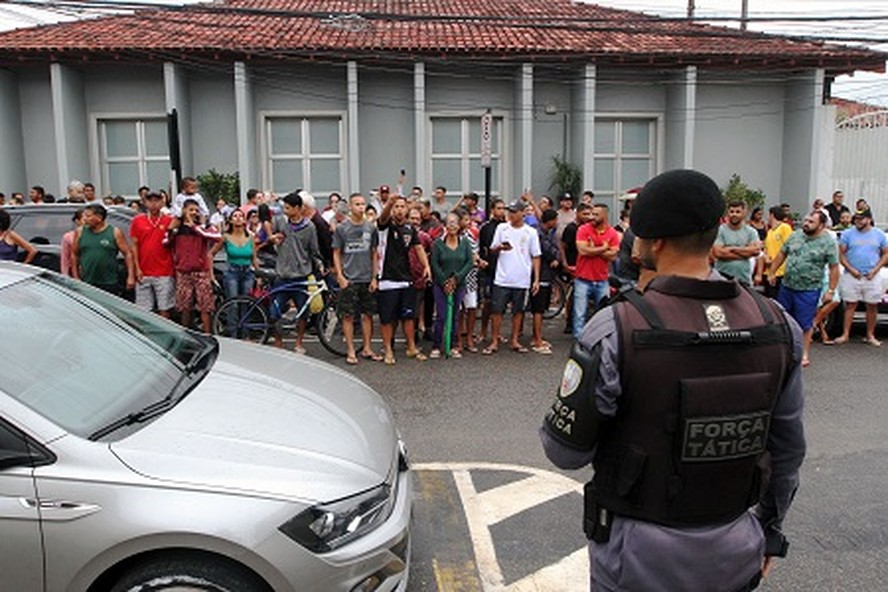 Policial diante de moradores de  Aracruz reunidos em frente a delegacia onde adolescente que realizou ataques foi levado depois de apreendido
