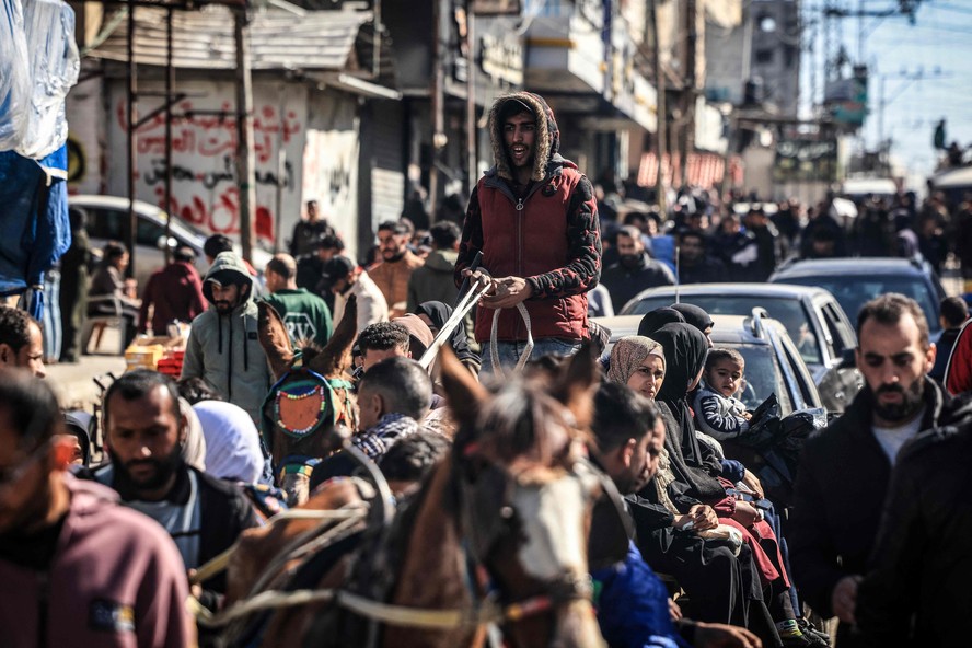 Deslocados pela guerra na Faixa de Gaza caminham por rua superlotada em Rafah