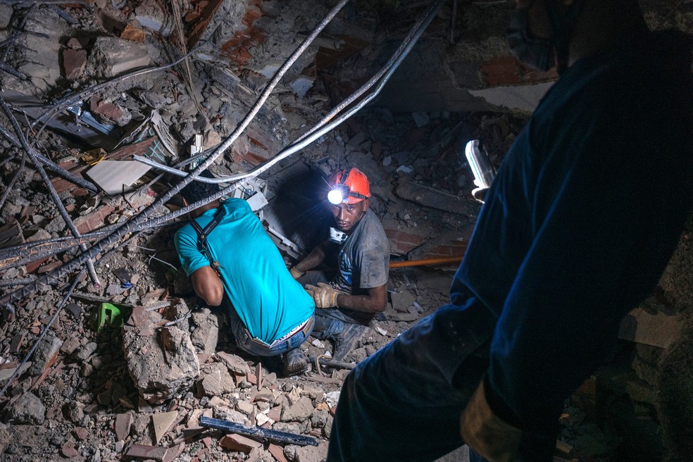 Dois homens ajoelhados removiam escombros com as mãos no complexo OPPE 33 — Foto: Adriana Loureiro Fernandez/NYT