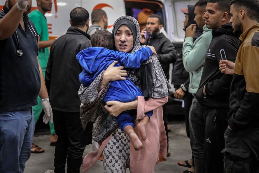 Mulher palestina corre com seu filho nos braços para o hospital em Gaza em novembro de 2023