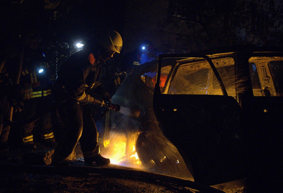 Bombeiros apagam incêndio em um carro atingido por bombardeio russo em Kiev — Foto: SERGEY SHESTAK / AFP