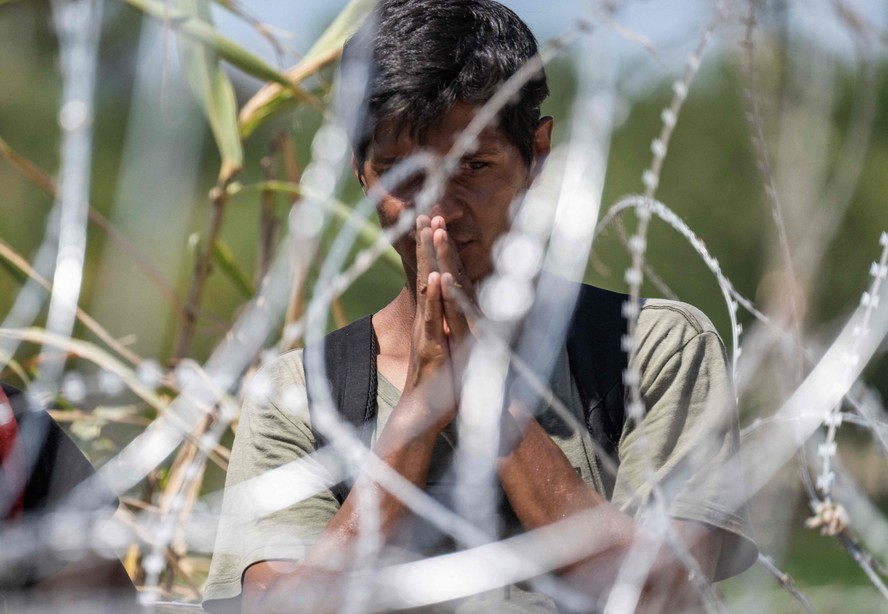 Um migrante venezuelano reza enquanto espera a interceptação dos agentes da Patrulha de Fronteira dos EUA depois que ele cruzou o Rio Grande para Eagle Pass, Texas