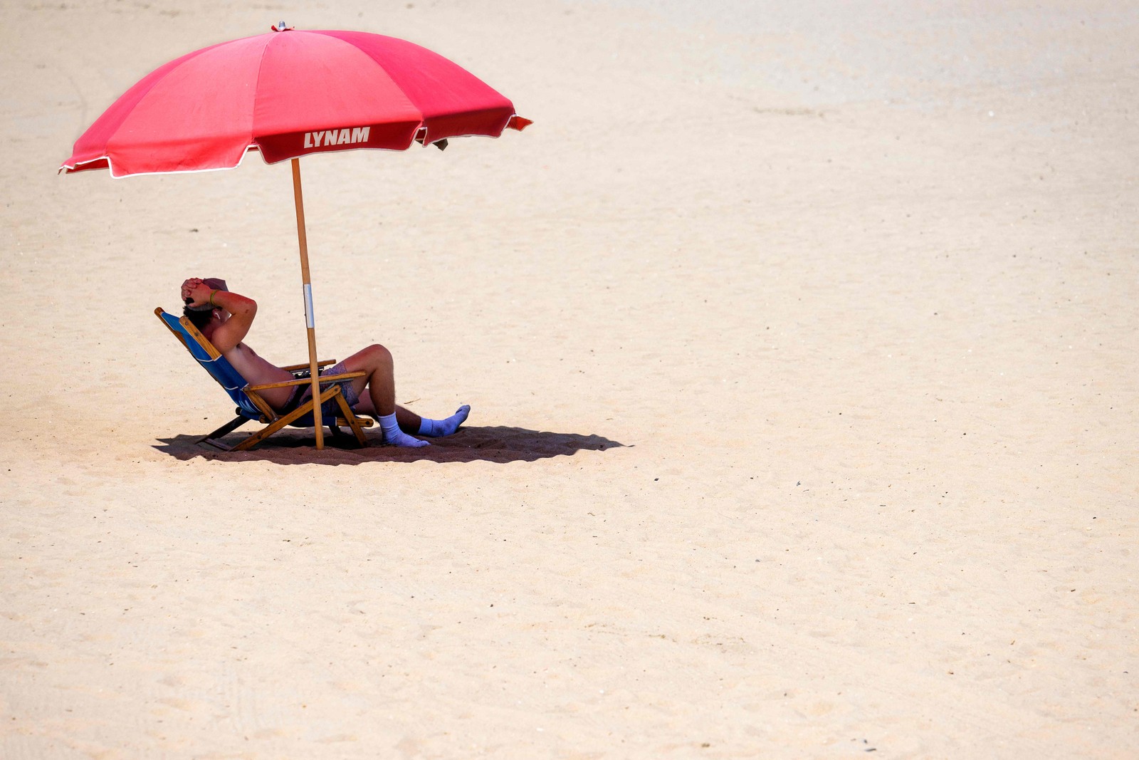Banhista encontra sombra sob um guarda-sol em Rehoboth Beach, em Delaware, EUA, em 28 de julho de 2023. Serviço Nacional de Meteorologia anunciou "calor opressivo" durante todo o fim de semana  — Foto: Jim WATSON / AFP