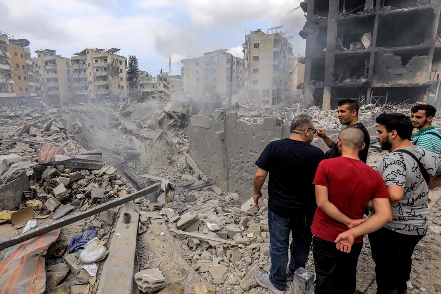 Pessoas inspecionam danos em uma cratera onde um prédio desmoronou após um ataque aéreo israelense  nos subúrbios ao sul de Beirute