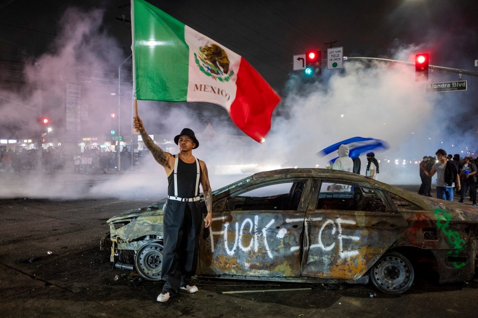 Manifestante segura bandeira do México em frente a pichação contra o Serviço de Imigração e Alfândega dos EUA (ICE, na sigla em inglês) em Los Angeles — Foto: RINGO CHIU / AFP