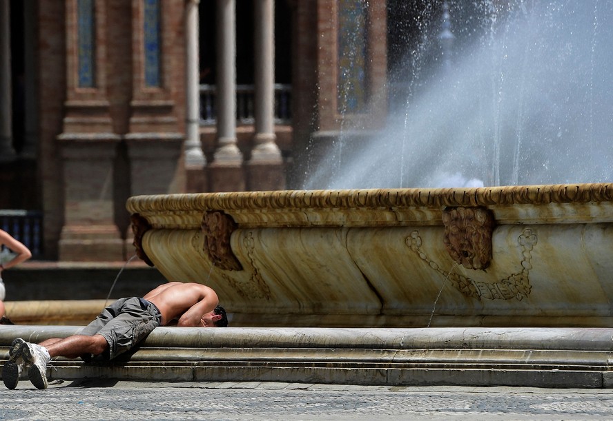 Jovem tenta se refrescar em fonte na Praça de Espanha, em Sevilha, em meio a onda de calor