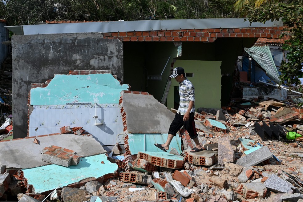Morador caminha sobre os escombros de uma estrutura destruída pelos fortes ventos na vila de pescadores de Nhon Hai, perto de Quy Nhon, após a passagem do tufão — Foto: NHAC NGUYEN / AFP
