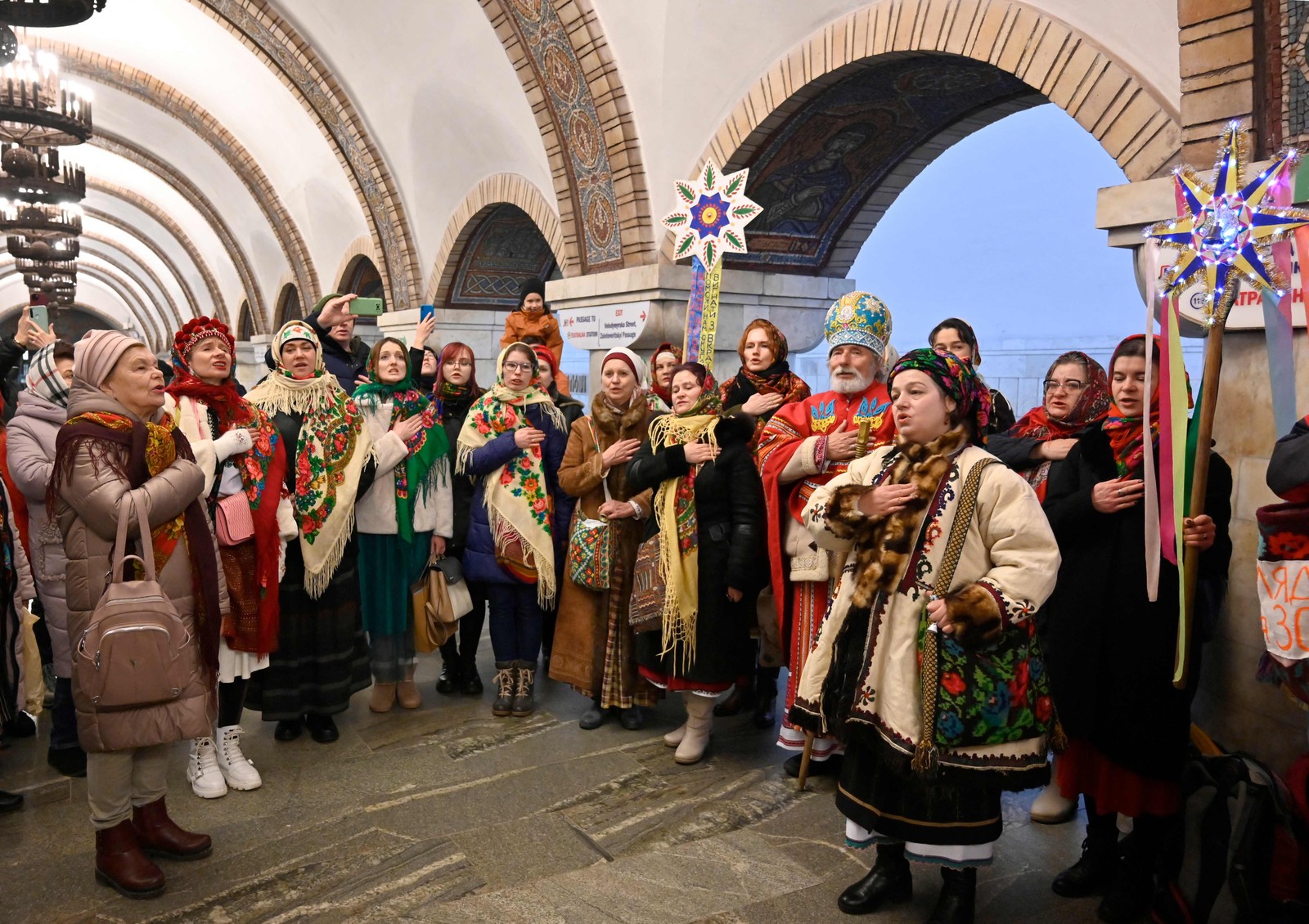 Moradores em trajes tradicionais cantam canções de Natal dentro de uma estação de metrô em Kyiv — Foto: SERGIO CHUZAVKOV/AFP