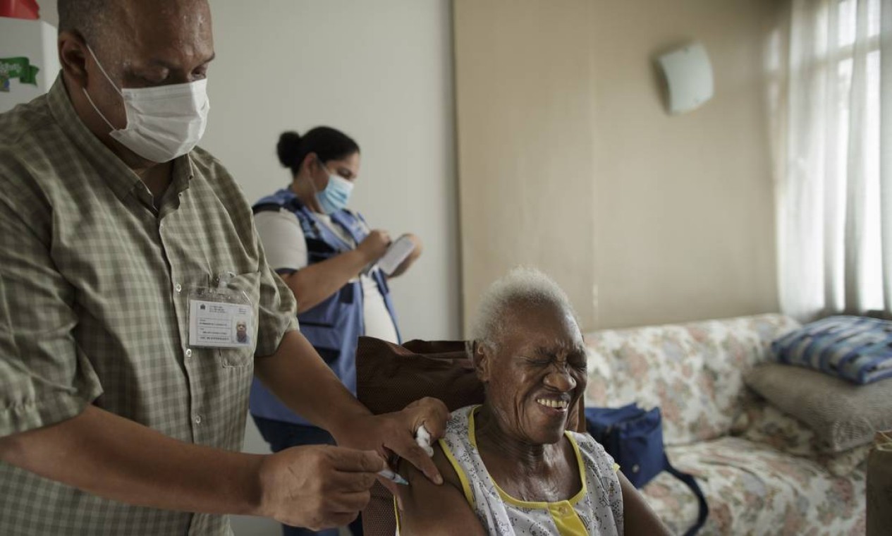 O técnico de enfermagem Milton Gomes Nunes Júnior aplica a vacina em Maria Palmira Maximiliano, de 87 anos, enquanto a agente comunitária Íris da Silva Brito preenche as carteirinhas de vacinação — Foto: Márcia Foletto / Agência O Globo