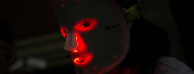 Visitante da feira usa uma máscara de luz vermelha da Light Tree Ventures — Foto: Brendan Smialowski / AFP