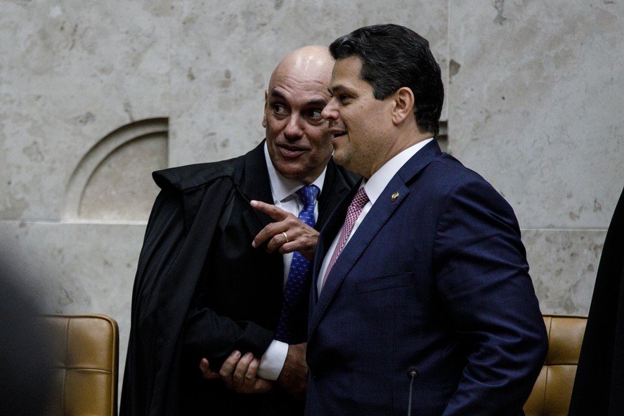 Davi Alcolumbre e o ministro Alexandre de Moraes conversando de cabeça baixa durante evento público em Brasília.