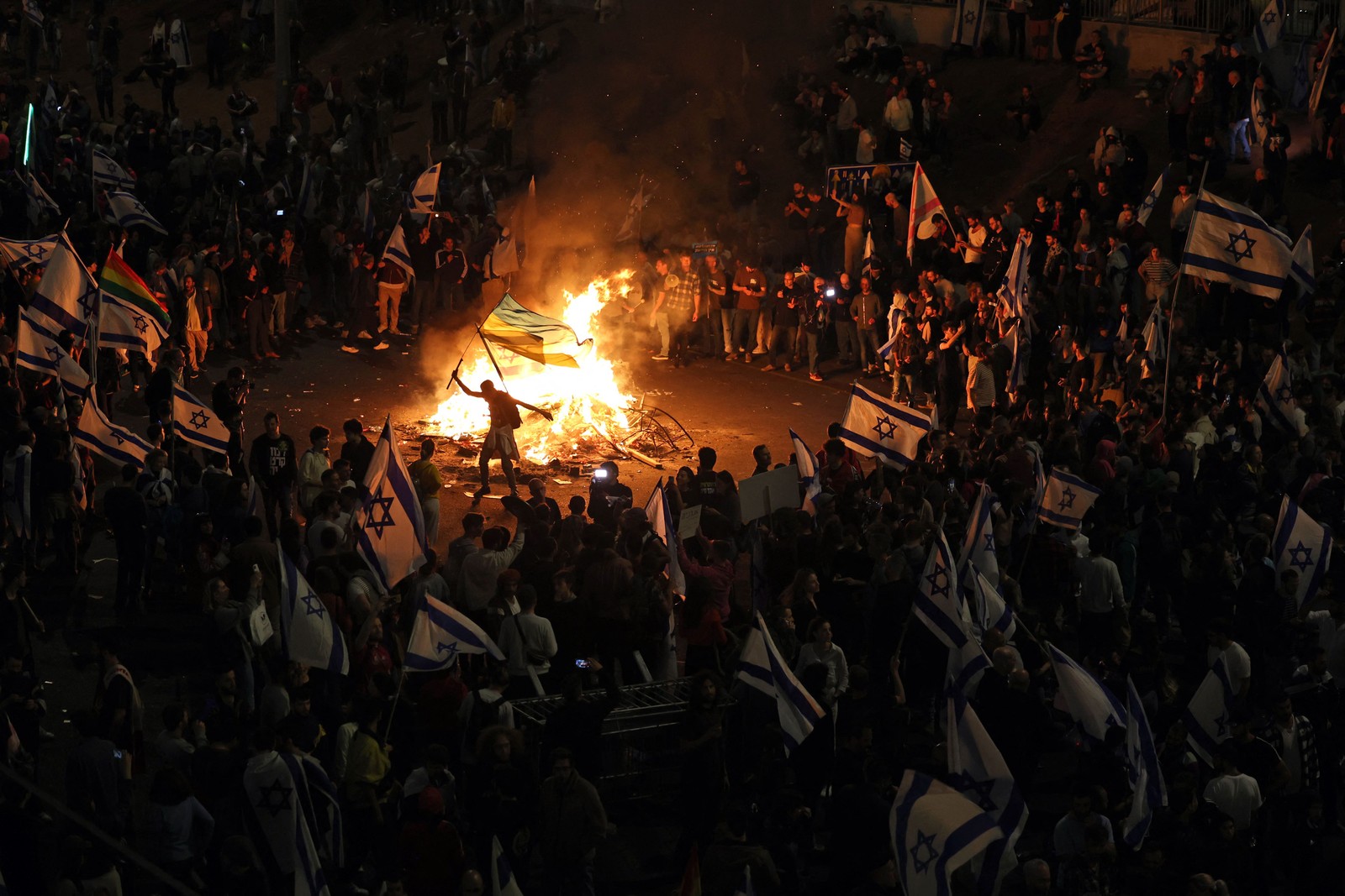 Manifestantes bloqueiam uma estrada e seguram bandeiras nacionais enquanto se reúnem em torno de uma fogueira durante uma manifestação contra a reforma judicial do governo israelense em Tel Aviv — Foto: AHMAD GHARABLI / AFP