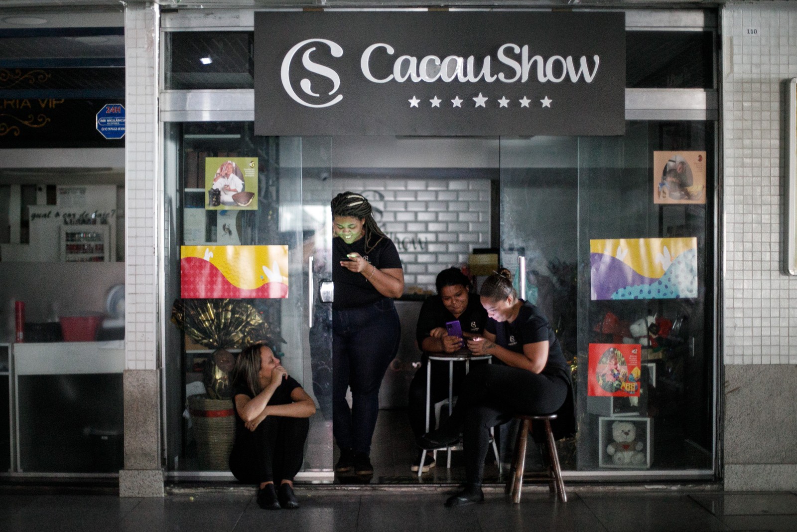 Funcionárias de loja de chocolate ficam atentas  ao celular em pausa forçada no trabalho devido a apagão — Foto: Brenno Carvalho/Agência O Globo