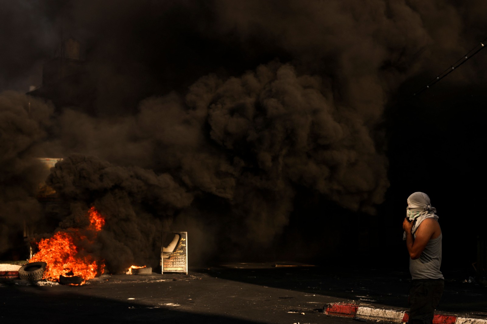 Homem mascarado caminha perto de uma barricada em chamas durante confrontos com o exército israelense na cidade ocupada de Jenin, na Cisjordânia, em 4 de julho de 2023 — Foto: RONALDO SCHEMIDT / AFP