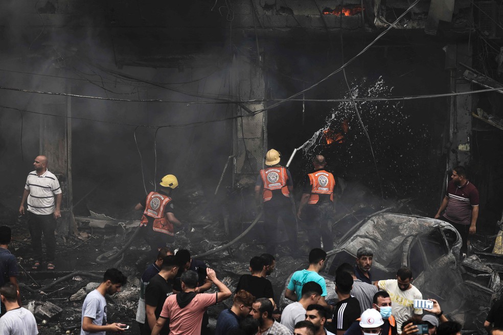 Bombeiros apagam chamas enquanto palestinos buscam por sobreviventes na Faixa de Gaza — Foto: Mohammed Abed/AFP