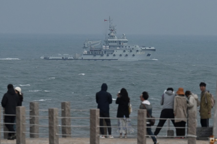 Navio da Marinha chinesa cruza pelo Estreito de Taiwan enquanto turistas passeiam na orla de Pingtan, parte do território chinês mais próxima de Taiwan