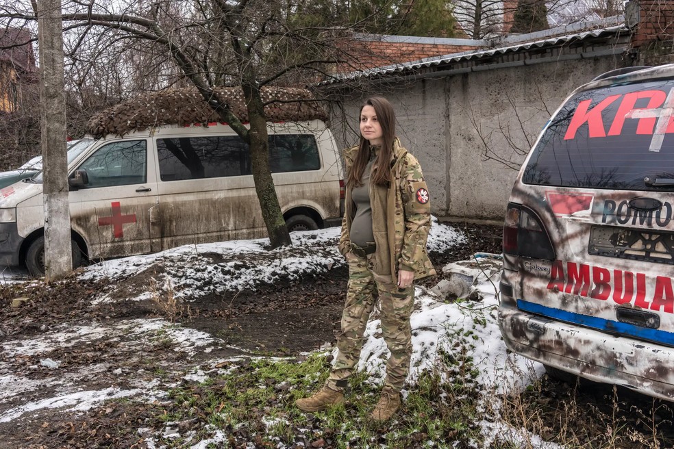 Olya, em Sloviansk, Ucrânia, em janeiro, não conseguia mais abotoar as calças e aguardava um uniforme de maternidade de Zemliachky. Médica de combate, ela disse que ia "com os rapazes para todas as posições de combate, para as trincheiras" em um Nissan Pathfinder coberto de lama, com as portas laterais abarrotadas de torniquetes e gloss labial no console central — Foto: Brendan Hoffman / The New York Times