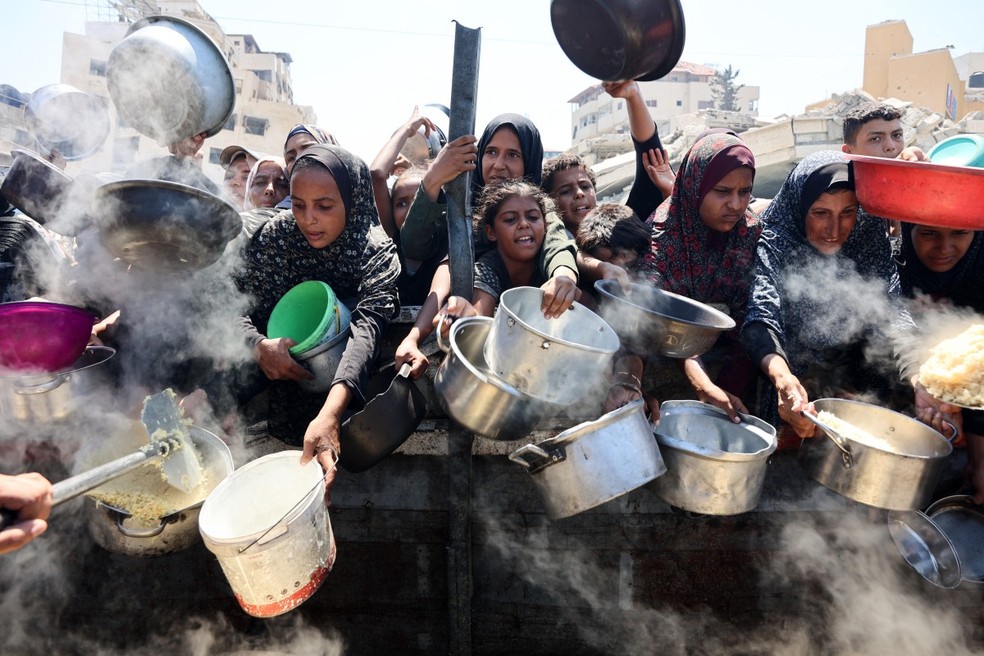 Mulheres e meninas palestinas se esforçam para receber arroz cozido de uma cozinha beneficente na Cidade de Gaza — Foto: Omar AL-QATTAA / AFP