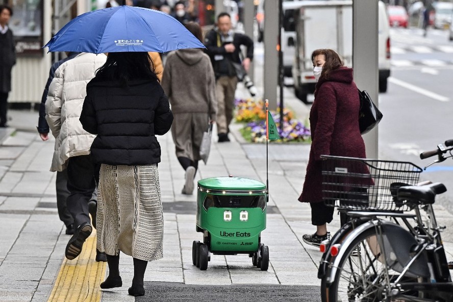 Pedestres caminham ao lado de um robô enquanto ele navega por uma rua durante demonstração de um serviço de entrega de robôs da Uber Eats Japan, em Tóquio