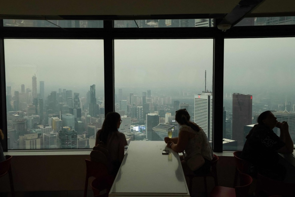 Pessoas observam a paisagem a partir da CN Tower enquanto a fumaça dos incêndios florestais no norte de Ontário encobre a cidade, causando má qualidade do ar, em Toronto, Ontário, Canadá, em 15 de julho de 2026. Toronto registrou a pior qualidade do ar entre as grandes cidades do mundo na quarta-feira, segundo a empresa suíça IQAir, enquanto as autoridades canadenses recomendaram que a população permanecesse em locais fechados. Toronto superou Nova Délhi e Kinshasa, capital da República Democrática do Congo, à medida que a fumaça dos incêndios florestais deixou o céu da maior cidade do Canadá com uma coloração amarelada-acinzentada e aspecto nebuloso — Foto: Cole BURSTON / AFP