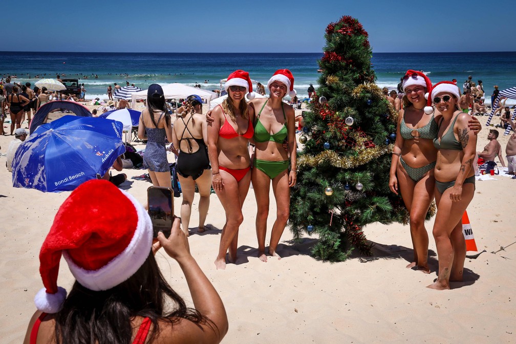 Turistas usando gorros posam para uma foto ao lado de uma árvore de Natal, em Bondi Beach, Sydney — Foto: AFP/Avid Gray