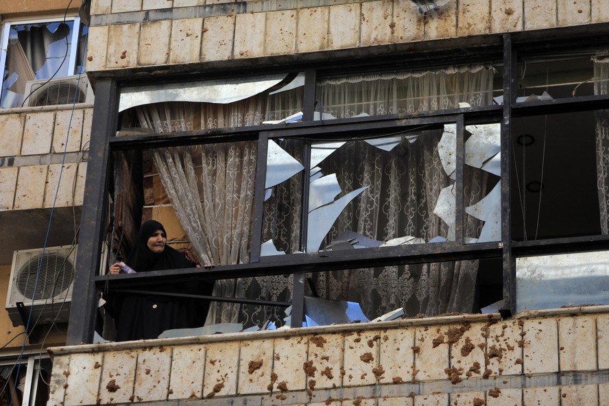 Mulher observa da janela quebrada perto de um prédio alvo de um ataque israelense nos subúrbios ao sul de Beirute