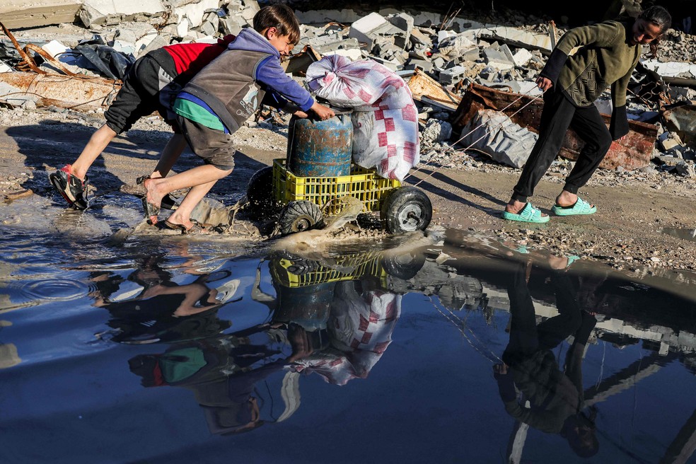 Criança empurra carrinho em rua destroçada da Cidade de Gaza — Foto: BASHAR TALEB / AFP